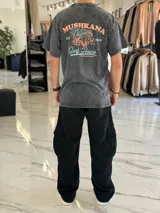 Remera oversize gris con efecto gastado, de manga corta, con estampa en la espalda de estilo surf con la inscripción "Mushkana Surf House".