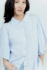 Camisa de lino color tostado, con cuello camisero y cierre frontal de botones. Se caracteriza por sus mangas cortas amplias y voluminosas que aportan un diseño fresco y liviano.