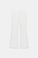Pantalón de tiro medio color blanco, de corte flare y acabado evasé, con detalle de costura lateral y cierre frontal con cremallera oculta.