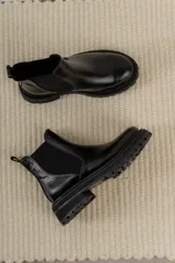 Bota Chelsea de cuero negro con elástico lateral y suela track.