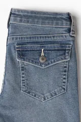 Jean de denim azul medio con leve efecto desgastado, corte ajustado hasta la rodilla y pierna acampanada (bootcut). Modelo de tiro bajo con cierre y botón, bolsillos abiertos delanteros y bolsillos traseros con solapa y botón.