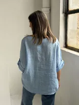 Blusa celeste de corte holgado, con cuello redondo, mangas tres cuartos con trabilla y detalles de alforzas en el frente.