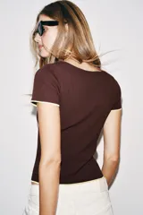 Top de punto color marrón con escote redondo amplio, manga corta y detalles de ribetes en color amarillo contrastante en el cuello, los puños y el ruedo.