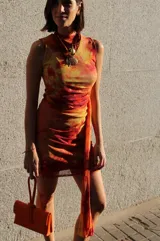 Vestido corto con estampado abstracto en tonos naranja, amarillo y rojo. Diseño ajustado al cuerpo, sin mangas y cuello redondo.