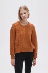 Sweater de tejido de punto color verde oliva, con cuello redondo y manga larga. Presenta un diseño de punto trenzado en el frente y mangas, contrastando con un tejido acanalado liso en el lado derecho del torso.