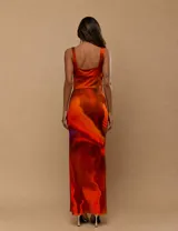Vestido largo de satén con estampado abstracto en tonos naranja y rojo. Presenta un escote tipo cowl, paneles laterales de microtul transparente en la cintura y una abertura lateral en la falda.
