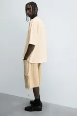 Bermuda de corte relajado en denim de algodón color beige, estilo cargo, con cinco bolsillos y bolsillos plastrón con solapa en las perneras.