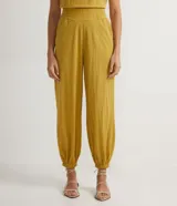 Pantalón harem color mostaza, con cintura elástica ancha, pliegues delanteros y horizontales, barra ajustada con elástico y pliegues.