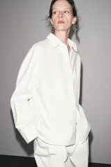 Sobrecamisa blanca de algodón con cuello solapa, manga larga y dos bolsillos de plastrón en el pecho. Cierre frontal con botones ocultos por solapa.