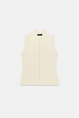 Top chaleco de punto color marfil, sin mangas, con escote en V y cuello alzado. Cuenta con cierre frontal de múltiples botones forrados a tono.