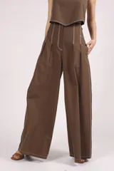 Pantalón marrón de corte palazzo, tiro alto, con pliegues frontales y pespuntes blancos decorativos.