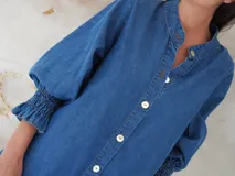 Vestido camisero de denim suave en tono celeste claro, con cuello mao, cierre frontal de botones y mangas tres cuartos con puños elásticos.