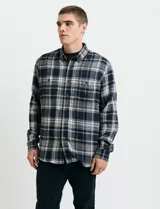 Camisa de franela a cuadros con cuello button-down, manga larga y botones de madera. Presenta dos bolsillos tipo parche en el frente con cierre de botón.
