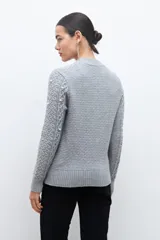 Sweater color beige melange de tejido de punto con diseño de trenzas y detalles de perlas en el frente y las mangas.