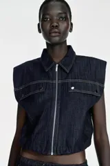 Chaleco de denim azul oscuro con cuello solapa, cierre frontal con cremallera y bajo elástico abullonado. Presenta tapetas delanteras y costuras en contraste.
