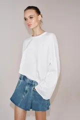 Falda corta de tiro medio confeccionada en tejido denim de algodón. Presenta diseño con tablas, bolsillos delanteros, cintura con trabillas y bajo desflecado. Cierre frontal con cremallera, botón y ganchos metálicos.