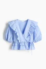 Blusa cruzada celeste a rayas blancas de popelina de algodón, con escote en V pronunciado, mangas cortas abullonadas, volados en el frente y detalle de lazo para atar en la cintura.