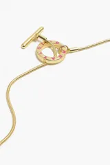 Collar dorado con cadena fina y dijes colgantes: un caramelo rosa y blanco, un pez tejido en tonos verde, amarillo y rosa, y un dije circular con letras rosas.