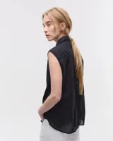 Camisa blanca sin mangas confeccionada en voile de algodón liviano. Tiene cuello camisero, cartera con botones de nácar, bolsillo plaqué en el delantero, costura en centro espalda y recorte en cintura trasera con tajo que se superpone. El ruedo es escalonado, más corto adelante.