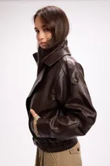 Campera estilo bomber oversize confeccionada en símil cuero negro con textura granulada. Presenta cuello alto con cierre frontal, hombreras marcadas, bolsillos laterales y cintura con elástico y cinto ajustable con hebilla metálica.