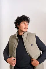 Chaleco puffer de corte regular, color beige, con cierre frontal y cuello alto. Presenta un diseño acolchado horizontal y logo bordado en el pecho.