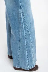 Jean de corte wide leg con tiro medio, confeccionado en denim de algodón. Presenta un diseño de pierna ancha con costuras verticales frontales que estilizan la silueta, cierre de botón y cremallera, y bolsillos clásicos.