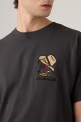 Remera negra de corte vintage con estampado de botas vaqueras y sombrero en el pecho.