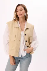 Chaleco estilo cargo color marrón, con cuello camisero, cierre frontal de botones negros y dos bolsillos frontales con solapa. Presenta detalles de terminaciones desflecadas en el ruedo y en los bolsillos.