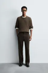 Jersey de punto color marrón oscuro, con cuello redondo y manga larga. Presenta un tejido con estructura de ochos y acabados en rib.