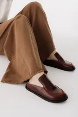 Zueco de cuero color marrón oscuro, con costuras decorativas en hilo rojo en el empeine y suela plana de goma.