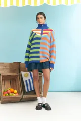 Sweater de tejido de punto grueso, cuello alto con cierre parcial y manga larga. Presenta un diseño de bloques de color y rayas horizontales en tonos vibrantes como azul, verde lima, naranja y celeste.