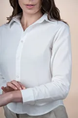 Camisa de algodón color blanco, con cuello camisero, cierre frontal con botones y mangas largas con puños abotonados.