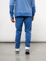 Pantalón deportivo de piqué color azul marino, con franjas laterales en contraste rojo y blanco. Presenta el escudo del Club Nacional de Football bordado en la pierna derecha y una etiqueta conmemorativa en la izquierda.