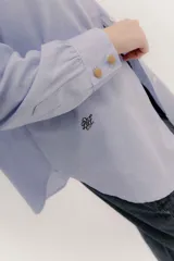 Camisa de manga larga color rosa claro con textura, cuello y puños blancos contrastantes. Los puños tienen tres botones rosados.