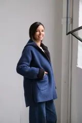 Tapado de paño azul con capucha, diseño de corte holgado y largo a la cadera. Presenta detalles en color negro en el interior, bordes y puños, con bolsillos frontales amplios y cierre frontal.
