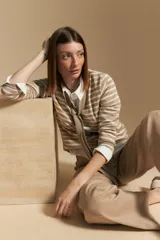 Cárdigan de tejido de punto a rayas horizontales beige y blanco, con escote en V y un lazo ancho anudado al frente. Se lleva sobre una camisa blanca de cuello abotonado con puños anchos.