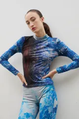 Polera de cuello alto y manga larga, confeccionada en tela sublimada con un estampado artístico que evoca un paisaje boscoso en tonos azules y marrones.