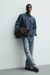 Camisa de corte relajado confeccionada en una mezcla de lyocell y algodón con efecto lavado. Presenta cuello solapa, manga larga con puños abotonados, bolsillo de plastrón en el pecho y cierre frontal con botones.