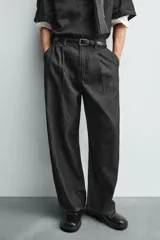 Pantalón de jeans de algodón ligero, color negro lavado, con corte balloon fit (holgado y ancho). Presenta pliegues frontales marcados en la cintura y cierre frontal de cremallera y botón.