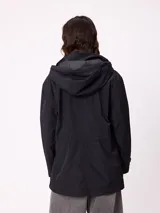 Rompevientos negro con capucha ajustable mediante cordones, cierre frontal de cremallera y ajuste en la cintura con cordón. Presenta logo de la marca bordado en el pecho y puños con detalle de botón.