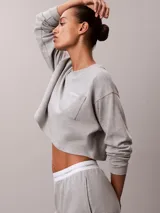 Top cropped de manga larga en tejido de punto de algodón color gris melange. Presenta cuello redondo, hombros caídos y un bolsillo de parche en el pecho con el logo de la marca bordado.