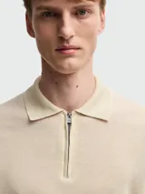 Remera polo de punto fino color beige, con cierre frontal parcial y cuello clásico. Presenta mangas cortas con terminación en rib y diseño de calce ajustado.