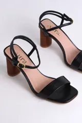 Sandalia de cuero color peltre, con tira ancha sobre los dedos y tira fina con hebilla al tobillo. El taco es cilíndrico de madera clara.