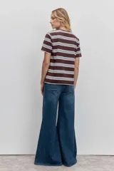 Remera de manga corta con cuello redondo, confeccionada en tejido de punto con diseño de rayas horizontales en tonos marrón, blanco y celeste. Presenta un pequeño parche circular rojo en el pecho.