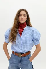 Camisa blanca de algodón con cuello mao, botonera oculta, mangas cortas estilo raglán con cortes estructurados y un bolsillo frontal con cierre.