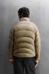 Campera puffer color beige con cuello alto, cierre frontal con cremallera y bolsillos laterales con cierre. Diseño acolchado horizontal.