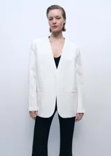 Chaqueta estructurada de corte recto y cuello de pico sin cierre. Presenta manga larga con aberturas en los puños, dos bolsillos de ribete laterales y una abertura posterior en el bajo. Incluye forro interior.