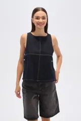 Musculosa de jean azul oscuro, de corte holgado, con cuello bote, pespuntes blancos y cierre lateral con botones metálicos.