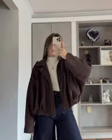 Campera tipo bomber de gamuza en color tostado, con diseño holgado, mangas amplias y cierre frontal con solapa.
