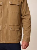 Campera de estilo safari en color azul marino, confeccionada en algodón. Presenta cuello alto, cierre frontal con cremallera y cuatro bolsillos delanteros con solapa y botones metálicos.